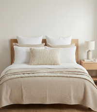 Neatly made bed with alpaca boucle cushion cover and other pillows in a bedroom setting.