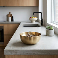 Gold bowl on a kitchen counter with a plant and fruit bowl in the background