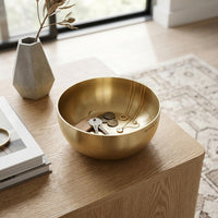 Gold jewelry bowl on a wooden surface with books and a vase in the background