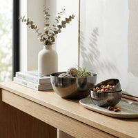 Decorative setup on a wooden surface with books, black nickel bowls, and plants.