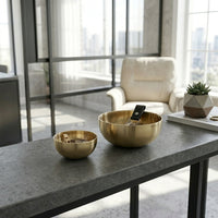 Two gold bowls on a gray table with a cityscape view in the background