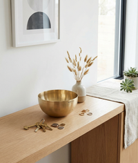 Small brass bowl on a wooden surface with decorative items and a window in the background