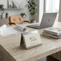 BEHR & CO cards on stainless steel card holder with laptop and books on a light marble surface.