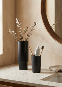 Bathroom counter with black vase, toothbrush holder, and mirror