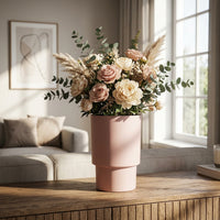 Pink vase with flowers on a wooden table in a living room.