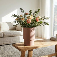 Pink vase with flowers on a wooden coffee table in a living room.