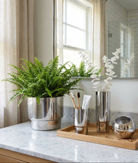 Modern bathroom counter with silver planters, vases, and a wooden tray.