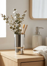 Bathroom counter with a metallic vase, toothbrushes, and soap dispenser.