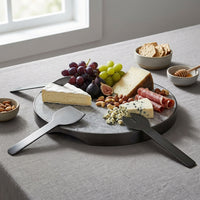 Cheeseboard with assorted cheeses, fruits, and meats on a gray table.