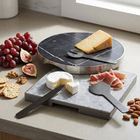 Cheese platter set with marble surface and black utensils on a kitchen counter.