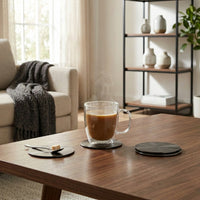 Clear mug with coffee on a black set of 4 coasters in a cozy living room.