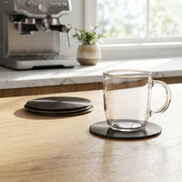 Clear glass mug on a coaster with a kitchen background featuring a coffee machine.