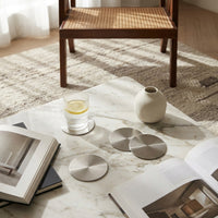 Marble coffee table with books, glass of water, and metallic coasters in a room with wooden chair and rug.