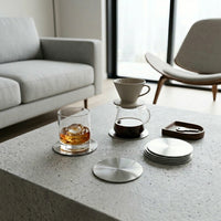 Modern living room with a coffee table featuring a glass of whiskey, coffee, and coasters.