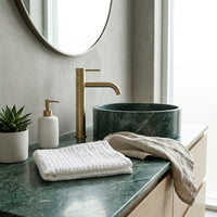 Bathroom vanity with marble countertop, organic facial cloth, gold faucet, and decorative items.