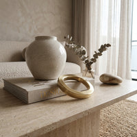 Decorative items on a stone surface including a vase, book, and gold ring.