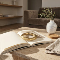Open book with a gold book weight on a wooden table in a cozy living room.