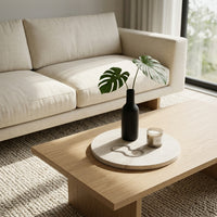 Beige sofa with a wooden coffee table featuring a black vase and candle on a stone jewelry tray.