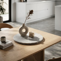 Decorative marble tray on a wooden table with a vase, candle, and books.