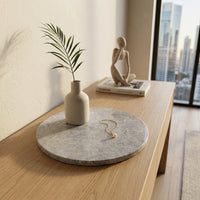 Decorative setting on a wooden table with a stone coaster, vase, plant, and statue.