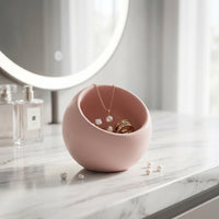 Pink jewelry holder with necklaces on a marble surface with a mirror in the background