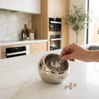 Person placing earrings into a metallic sphere on a kitchen counter