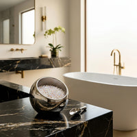 Bathroom scene with a bowl of bath salts in a salt holder on a marble counter, a bathtub, and a mirror.