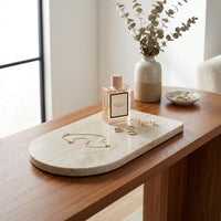 Gucci perfume bottle on a marble tray with jewelry, next to a vase with greenery on a wooden surface.